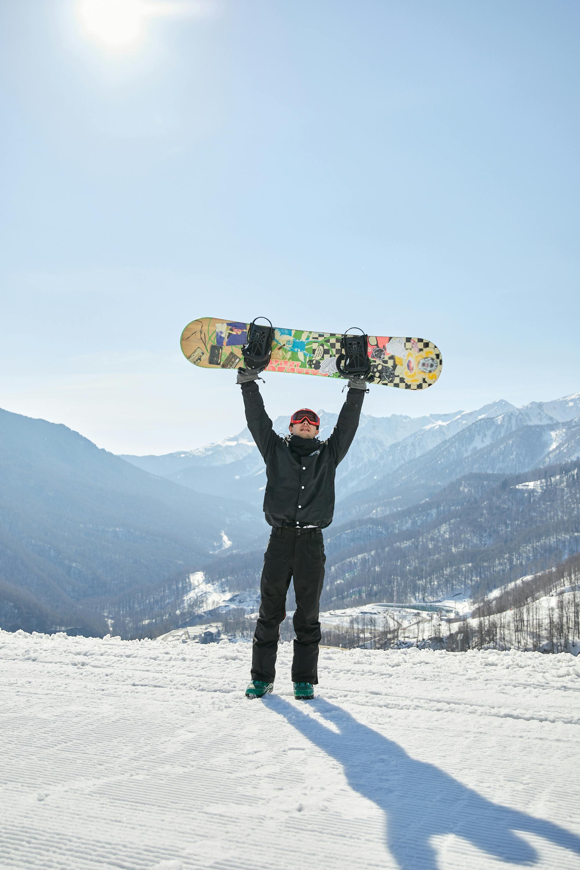 Prescription Goggle Inserts - Snowboarder in winter clothing holding snowboard overhead on scenic snowy mountain in Sochi, Russia.