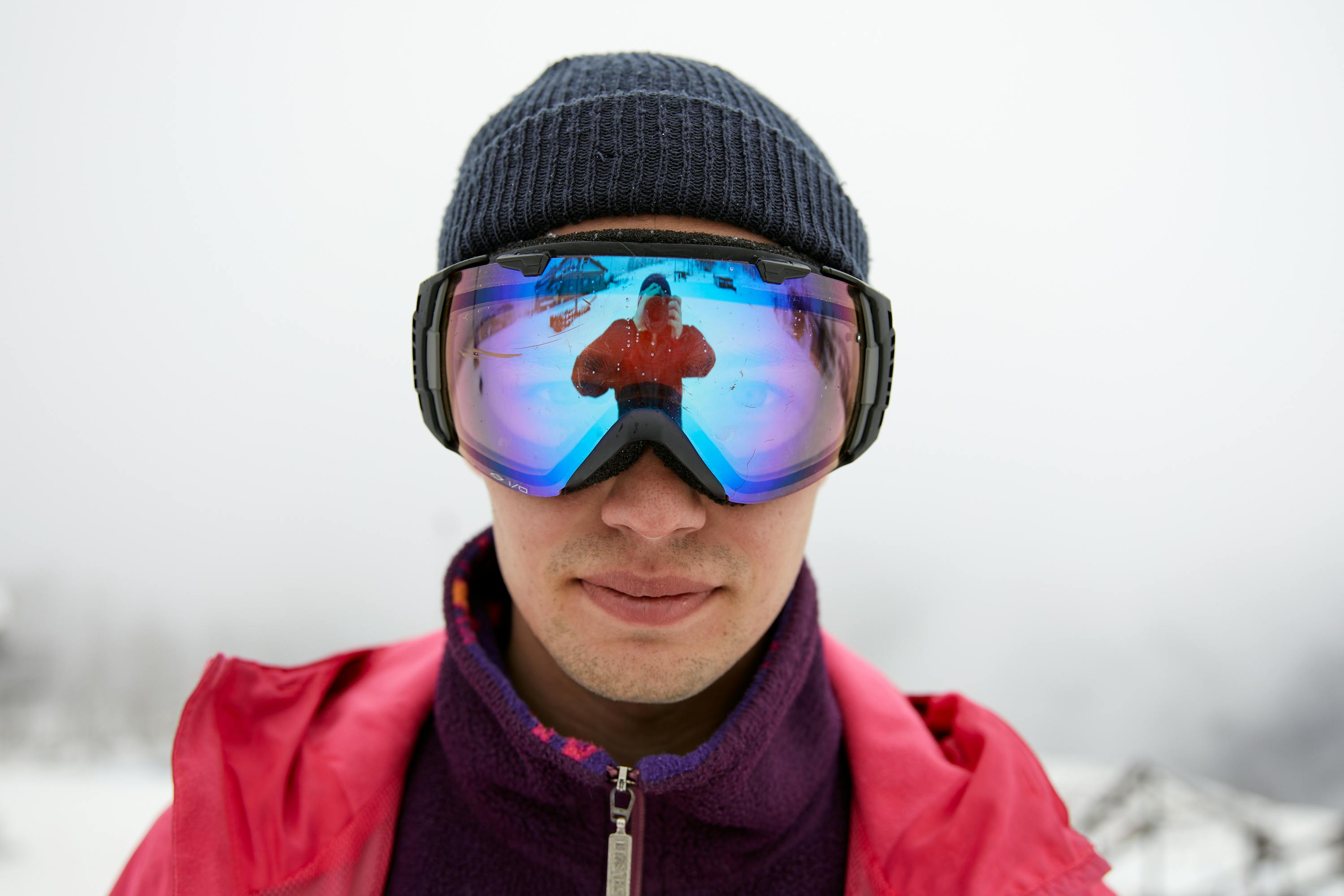 Close-up of a man in winter clothing with reflective snow goggles showing a reflection.