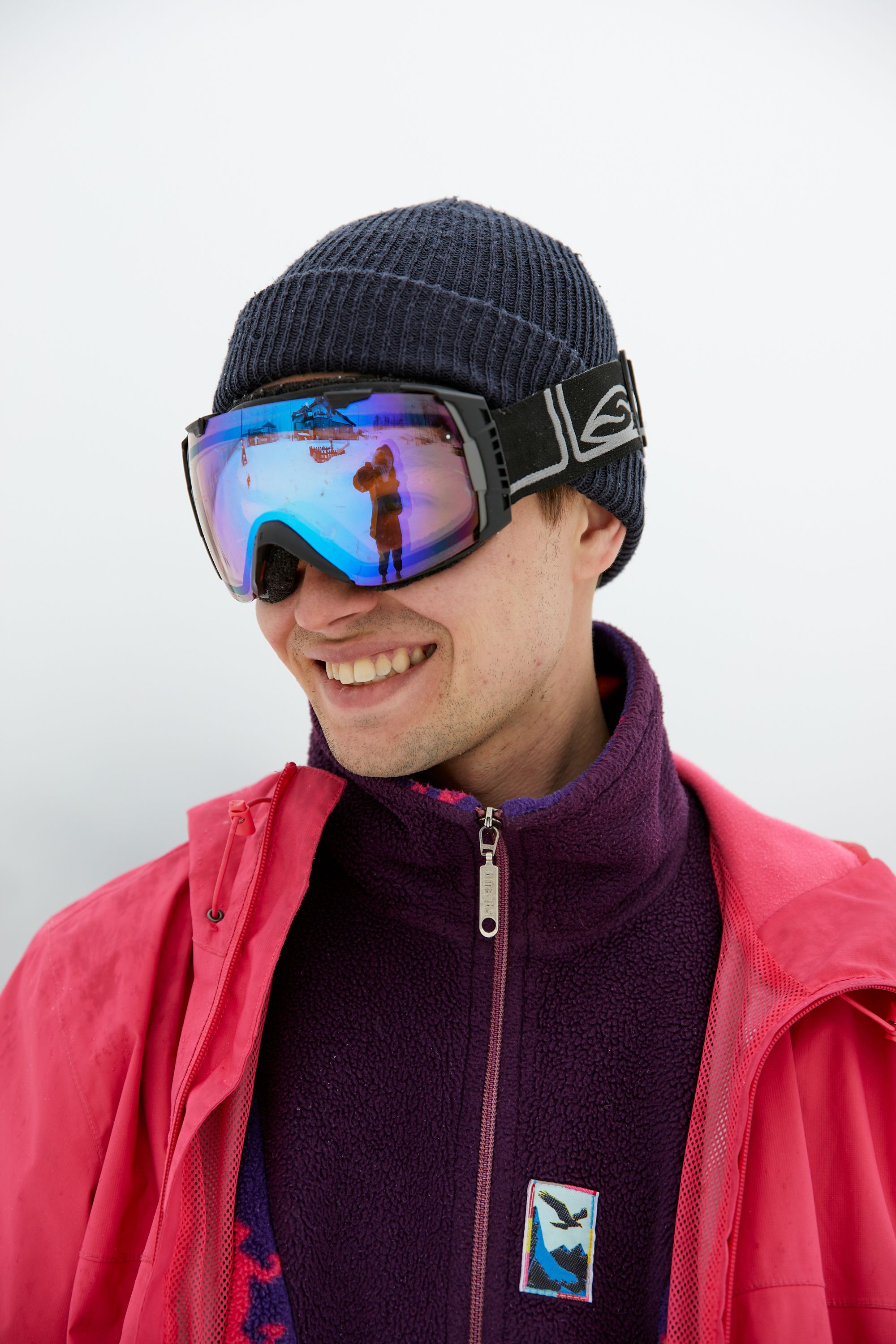 Portrait of a man outdoors in winter clothing, wearing reflective goggles and a beanie with a smile.