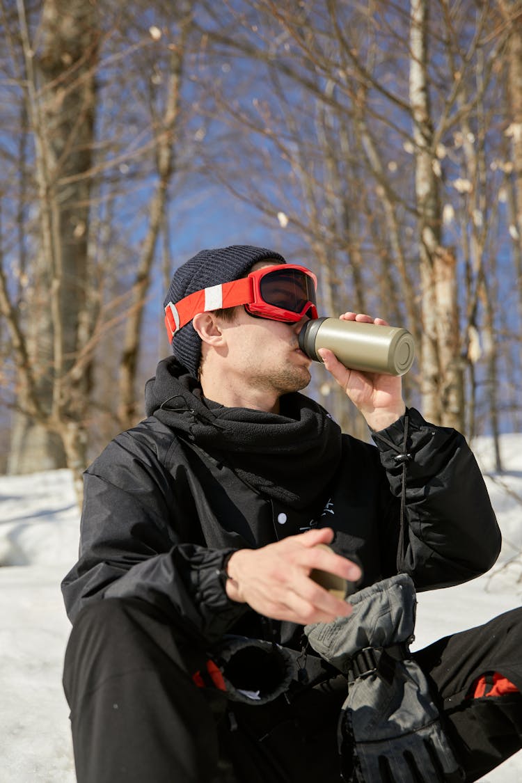 Snowboarder Sitting In Snow Drinking From Thermos