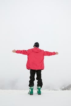 Man in winter clothing standing arms open on snowy landscape, embracing the cold season.