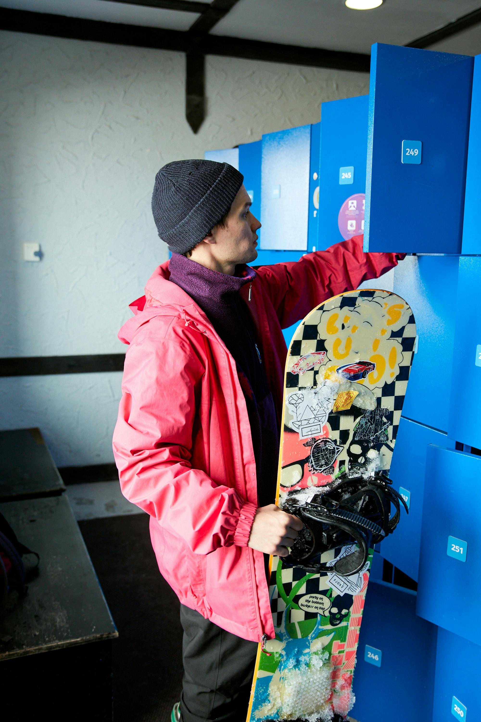 Adult man placing snowboard into locker, wearing winter clothing indoors.