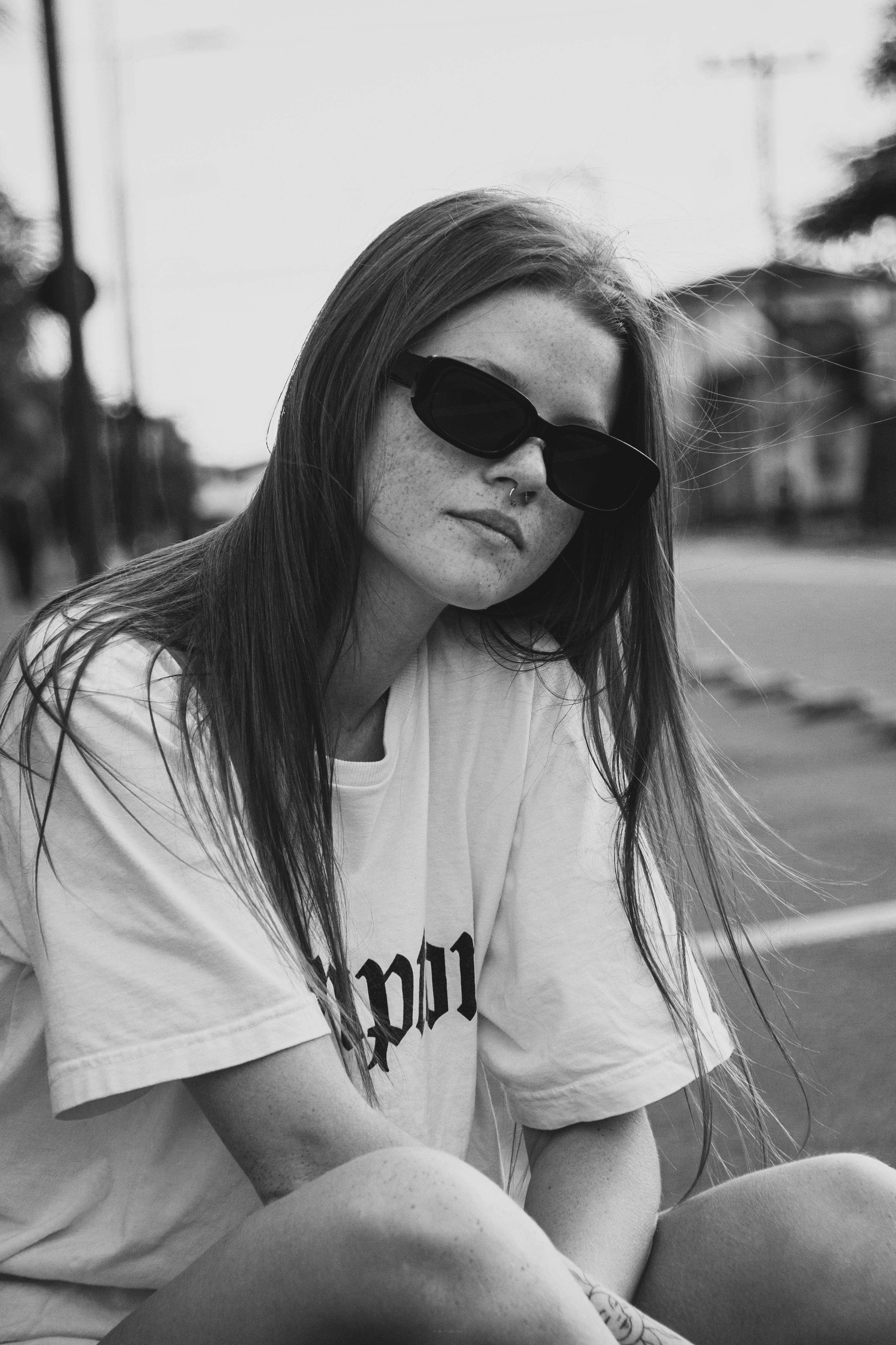 Black and white portrait of a woman wearing sunglasses, sitting outdoors.