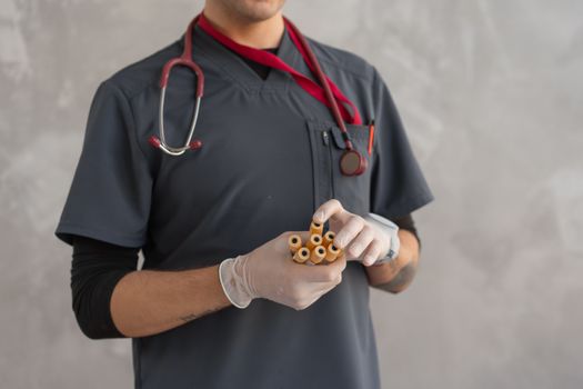 Close-up of a doctor in scrubs holding test tubes, equipped with a stethoscope and latex gloves.