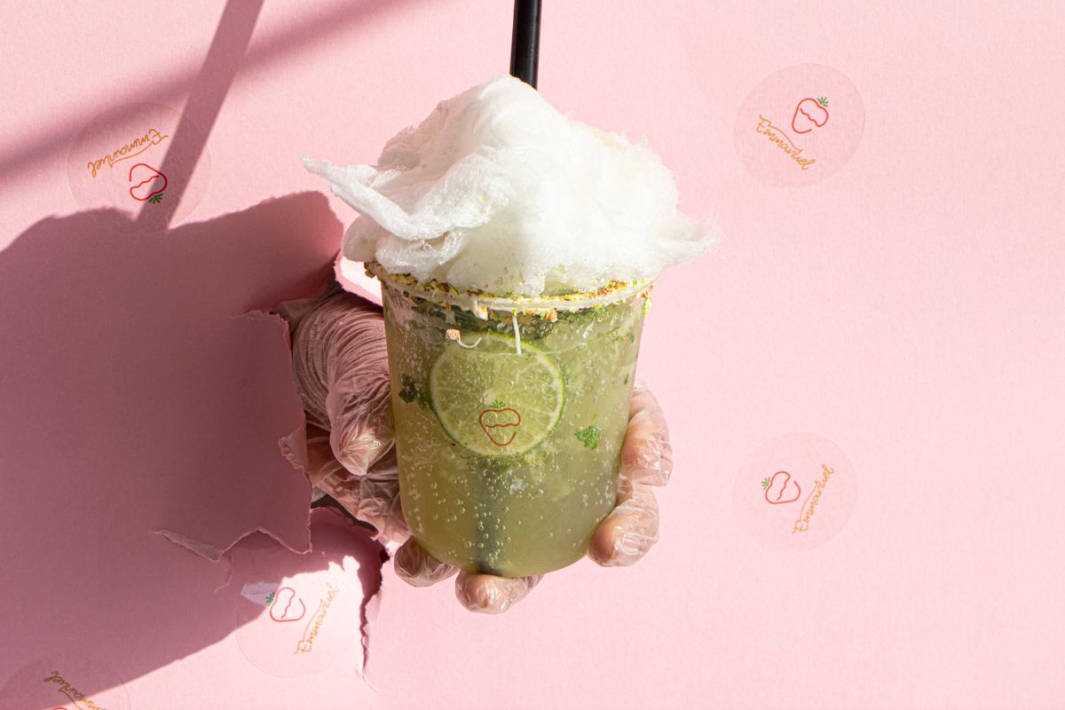 A hand holding a lime drink with cotton candy against a pink wall, symbolizing freshness.