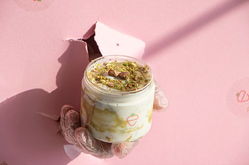 Free A hand holds a dessert jar with creamy yogurt and nuts against a pink background, offering a sweet treat. Stock Photo
