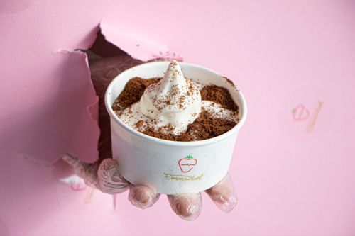 Free Hand holding ice cream topped with cocoa in a cup against a torn pink background. Stock Photo