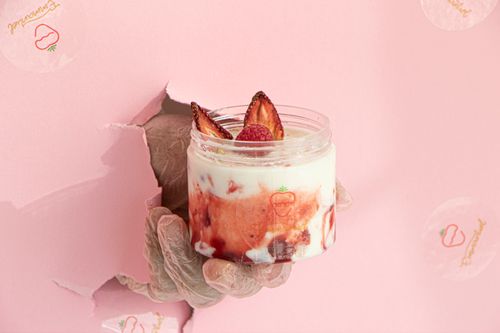 Free Close-up of a hand holding a yogurt cup with strawberries and raspberries against a pink background. Stock Photo