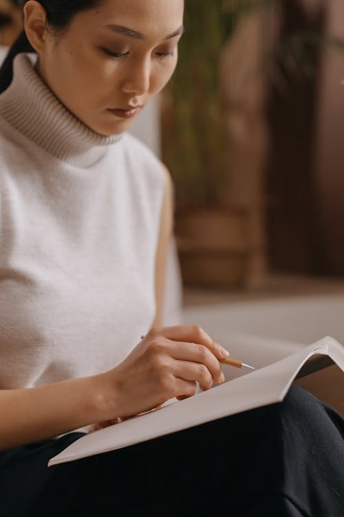 Free A Woman in White Turtleneck Writing on a Notebook Stock Photo