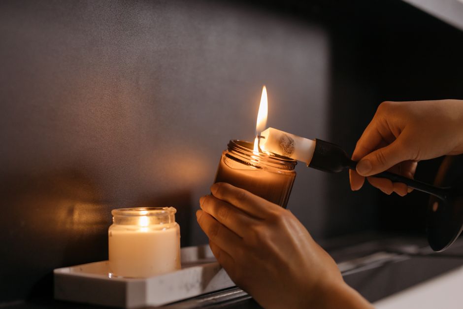 Close-up of hands lighting candles indoors, creating a warm cozy ambiance.