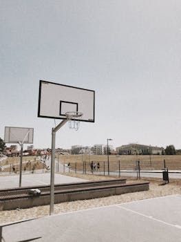 Low angle view of an outdoor basketball hoop in a sunny park with people walking nearby.