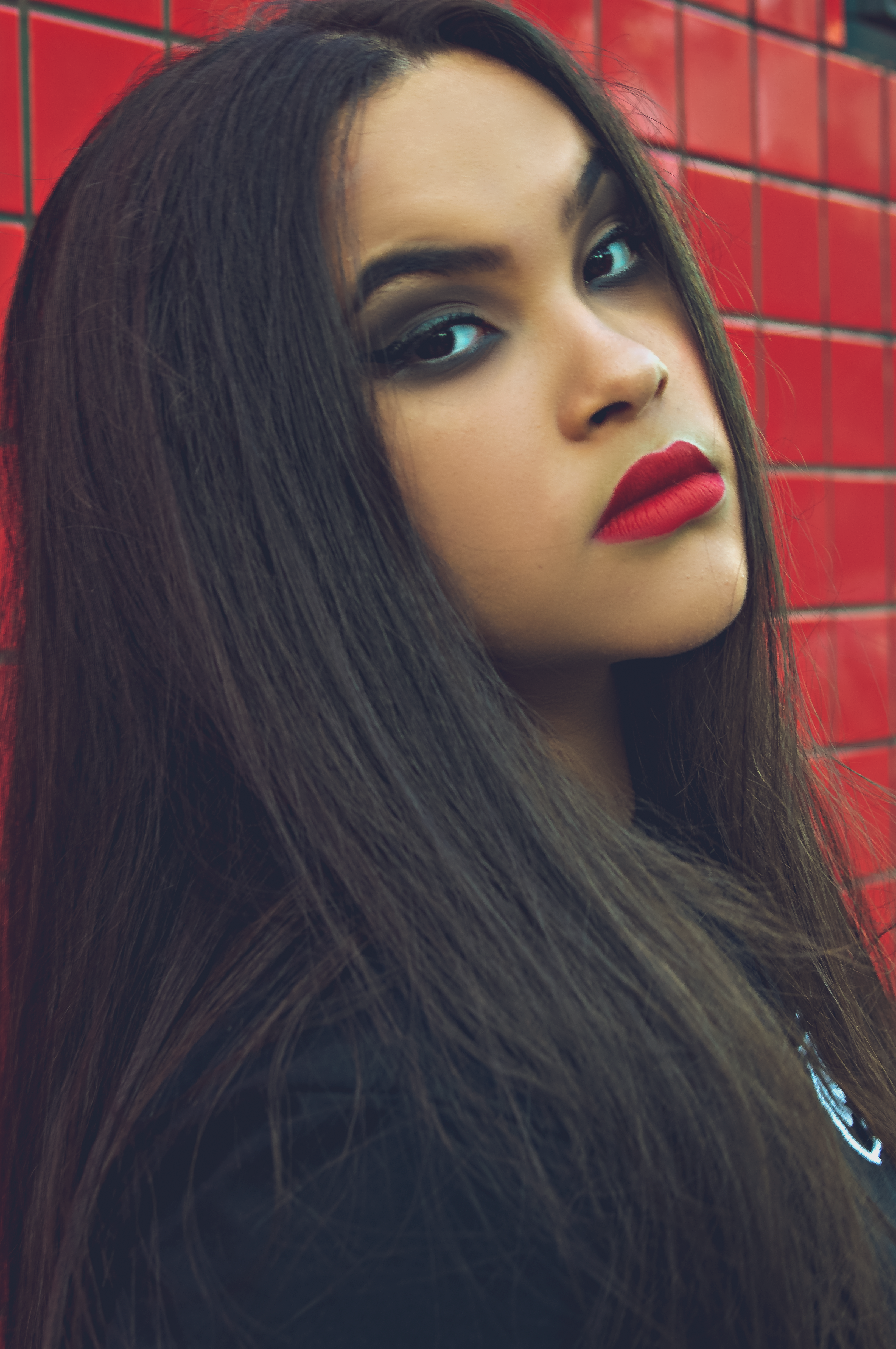 Captivating close-up portrait of a woman with bold red lips and striking makeup against a red tiled wall.