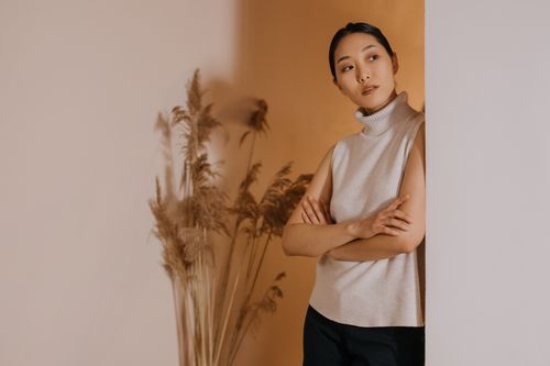 Free An Asian woman leans against a wall, posing elegantly with dried plants in a minimalist setting. Stock Photo