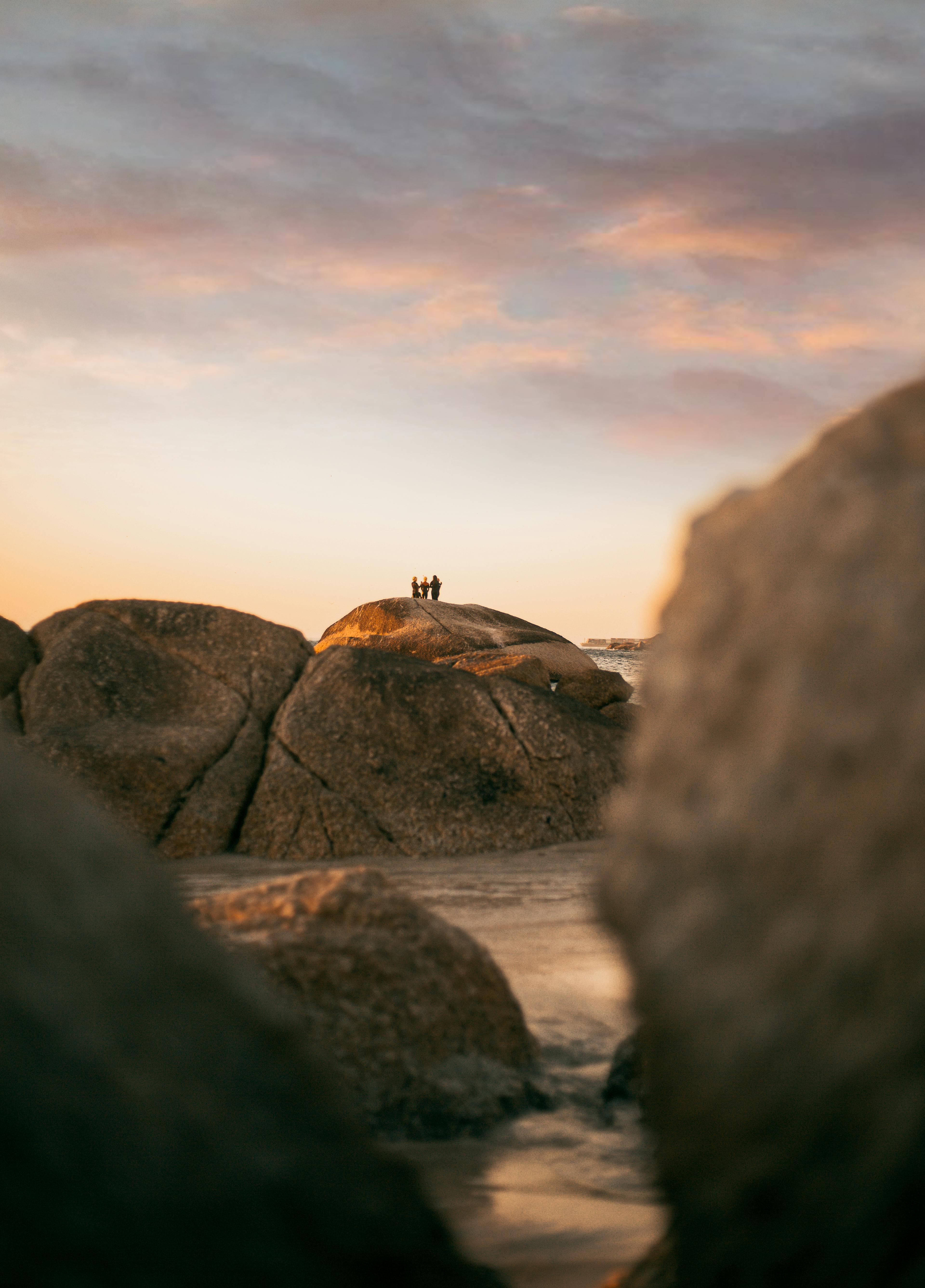 Silhouetted figures on boulders by the ocean during a golden sunset.