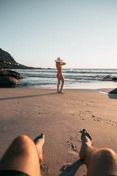 A relaxing beach scene with a woman in swimwear and a hat by the ocean.