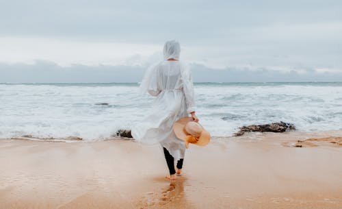 Free Back View of a Person in a White Dress Walking on the Sea Shore Stock Photo