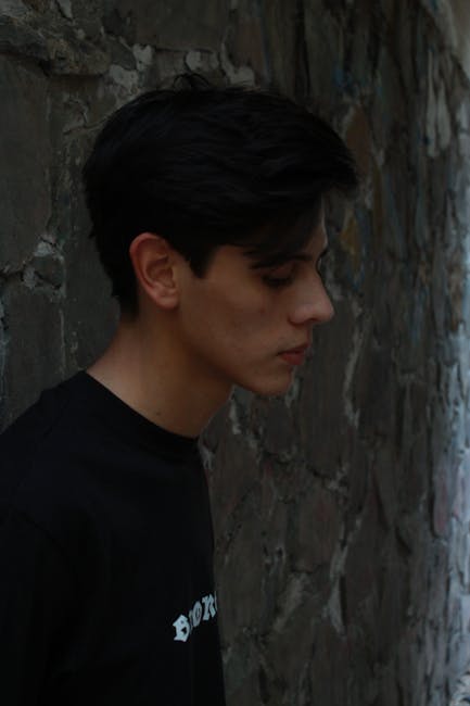 Side profile of a man in a black shirt leaning on a stone wall, captured outdoors.