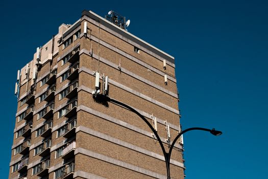 A low angle view of a tall building with antennas against a vibrant blue sky.