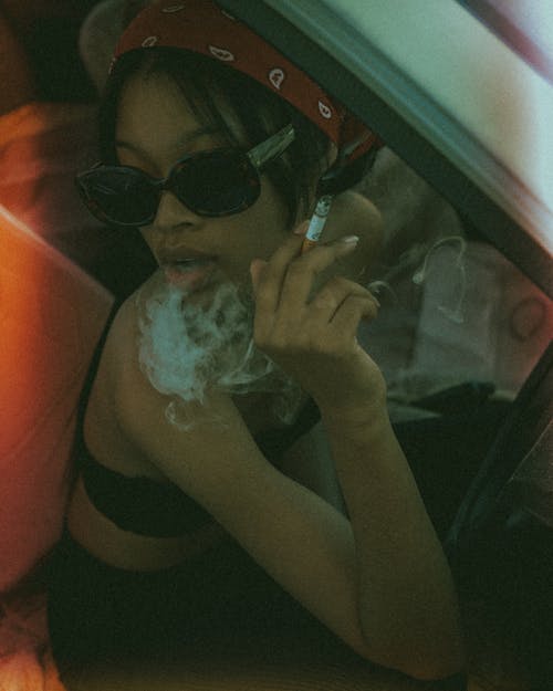 Close-Up Shot of a Woman Wearing Sunglasses While Smoking Cigarette