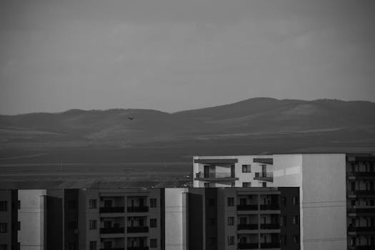 Black and white photo of urban apartments against distant rolling hills.