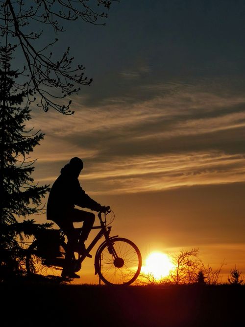 Free A cyclist silhouetted against a dramatic sunrise sky, creating a serene and natural scene. Stock Photo