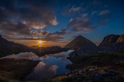 Serene sunrise over mountain lake with clouds reflecting in the water, creating a tranquil atmosphere.