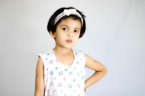 Free Adorable young girl with hand on waist, wearing a headband, posing confidently against a soft background. Stock Photo