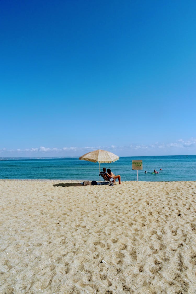 A Couple Sitting Under A Beach Umbrella