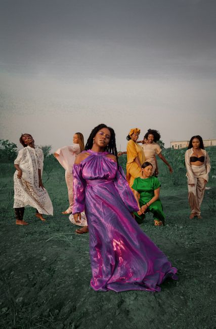 Group of diverse women posing in stylish dresses on a grassy outdoor setting.