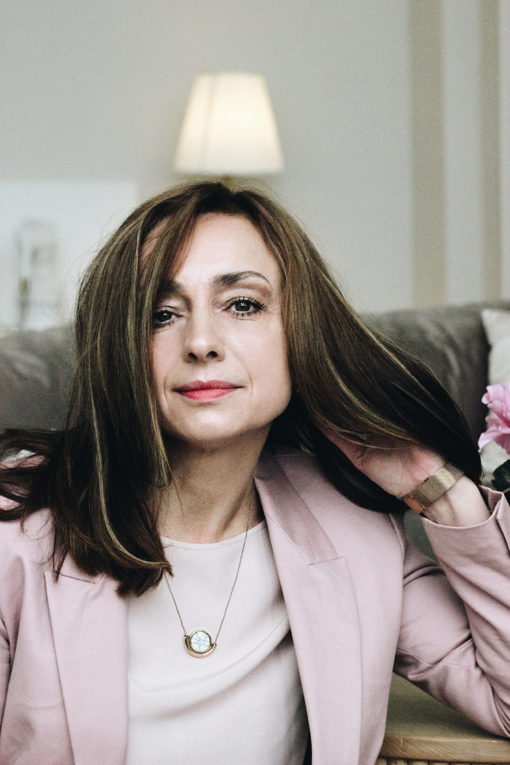 A sophisticated woman with long hair seated in a stylish indoor setting.