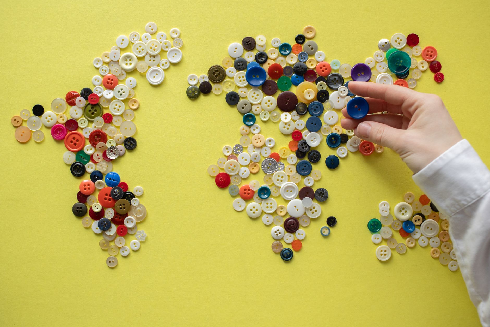 Colorful world map crafted from assorted buttons on a vibrant yellow background.