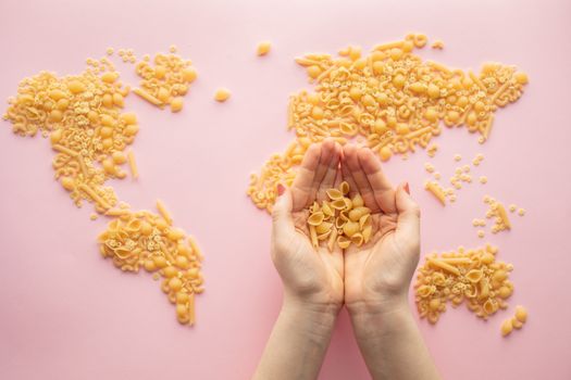 An artistic world map made from assorted pasta against a vibrant pink backdrop with hands holding pasta.