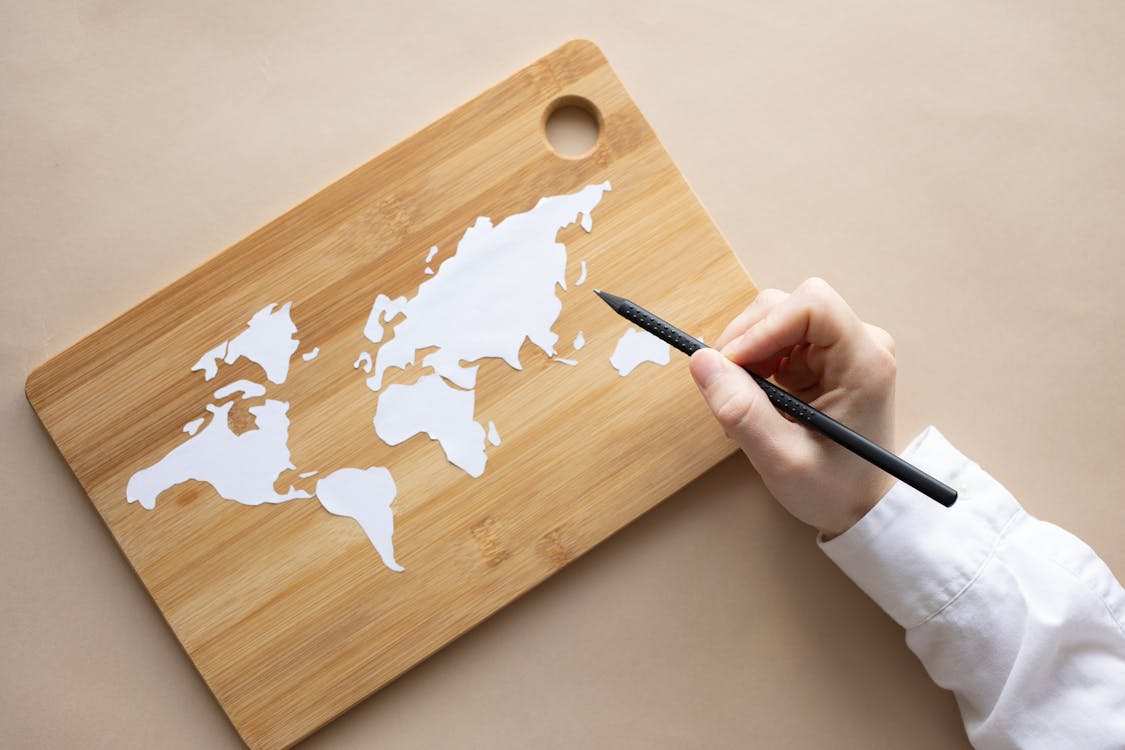 Crop artist with white pencil drawing world map on desk