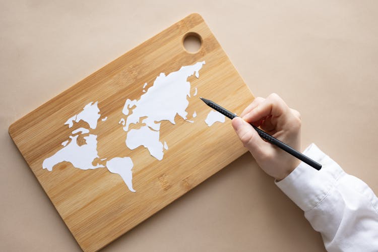 Crop Artist With White Pencil Drawing World Map On Desk