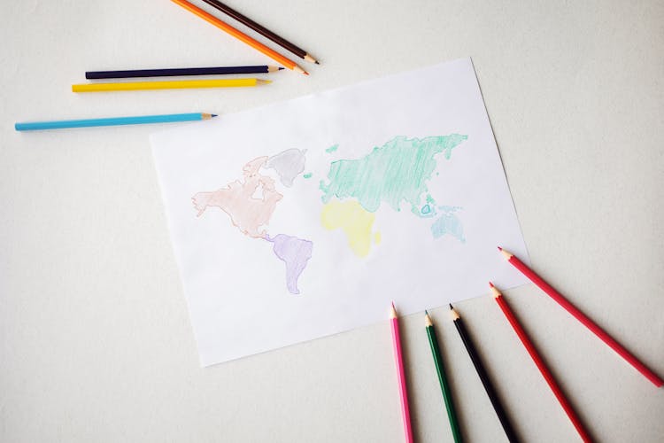 World Map Drawn On Paper Sheet Near Colorful Pencils