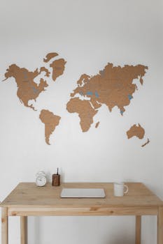Clean wooden desk with a world map wall, clock, cup, and book.