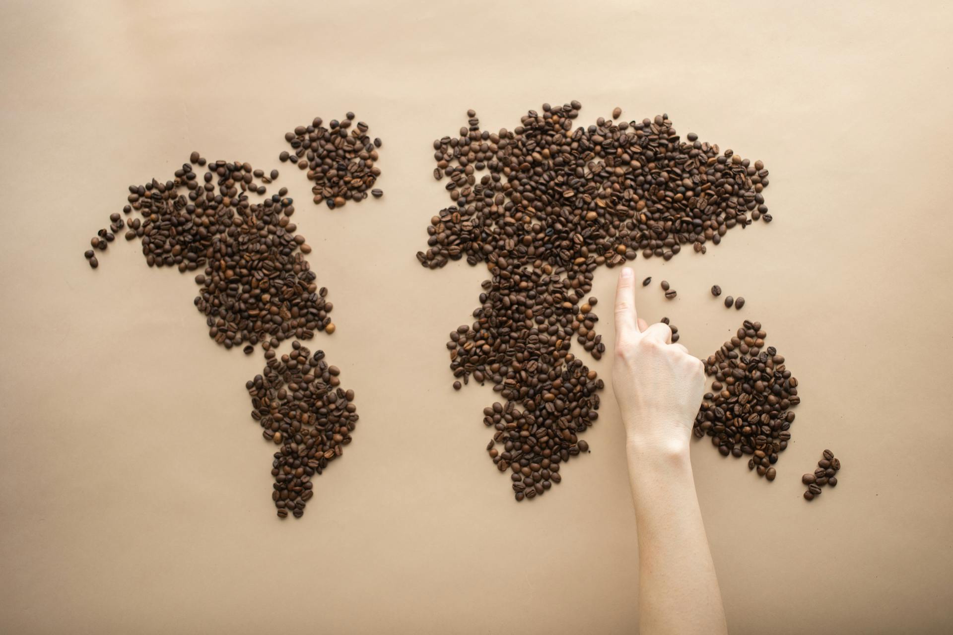 Top view of crop person pointing finger at world map made of coffee beans on brown background