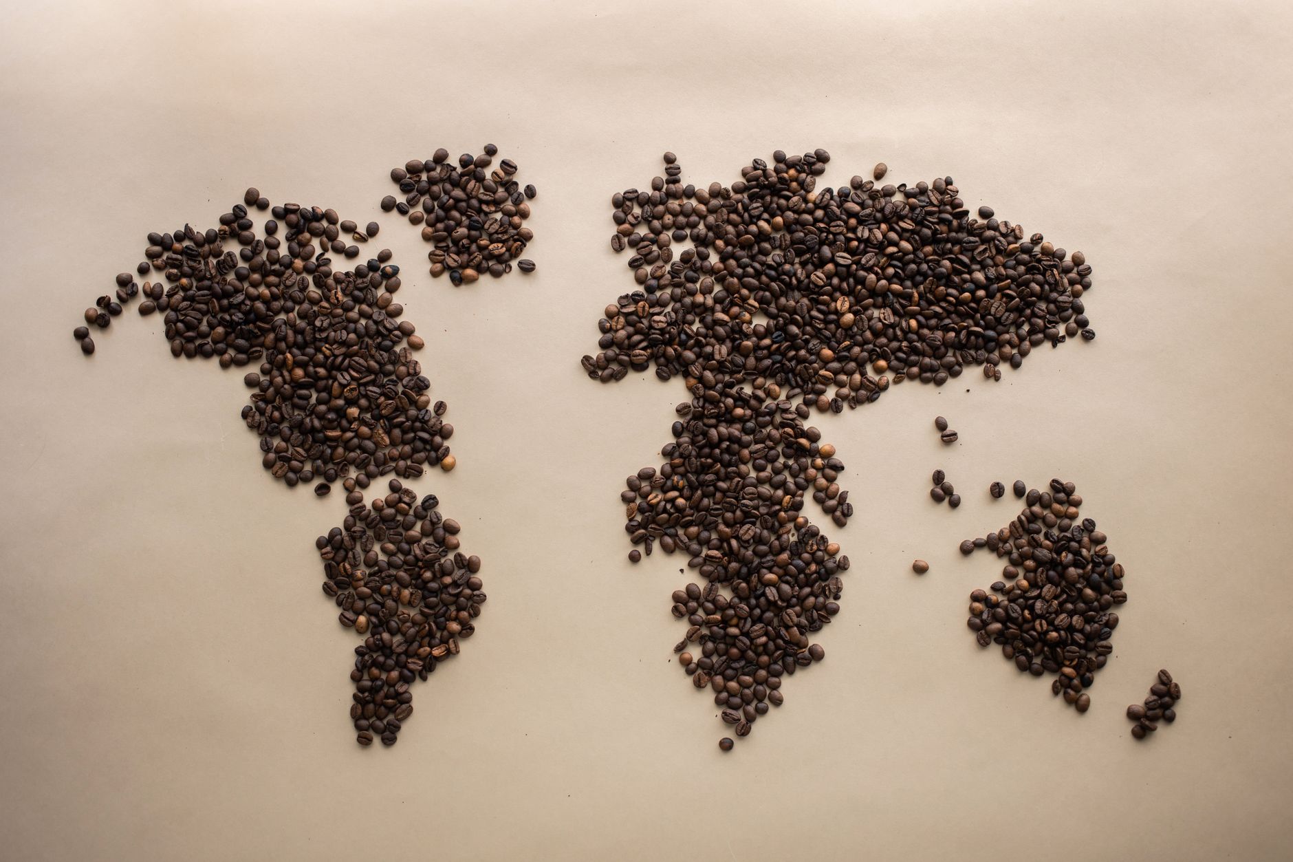 Creative world map design using coffee beans arranged on a beige background, top view
