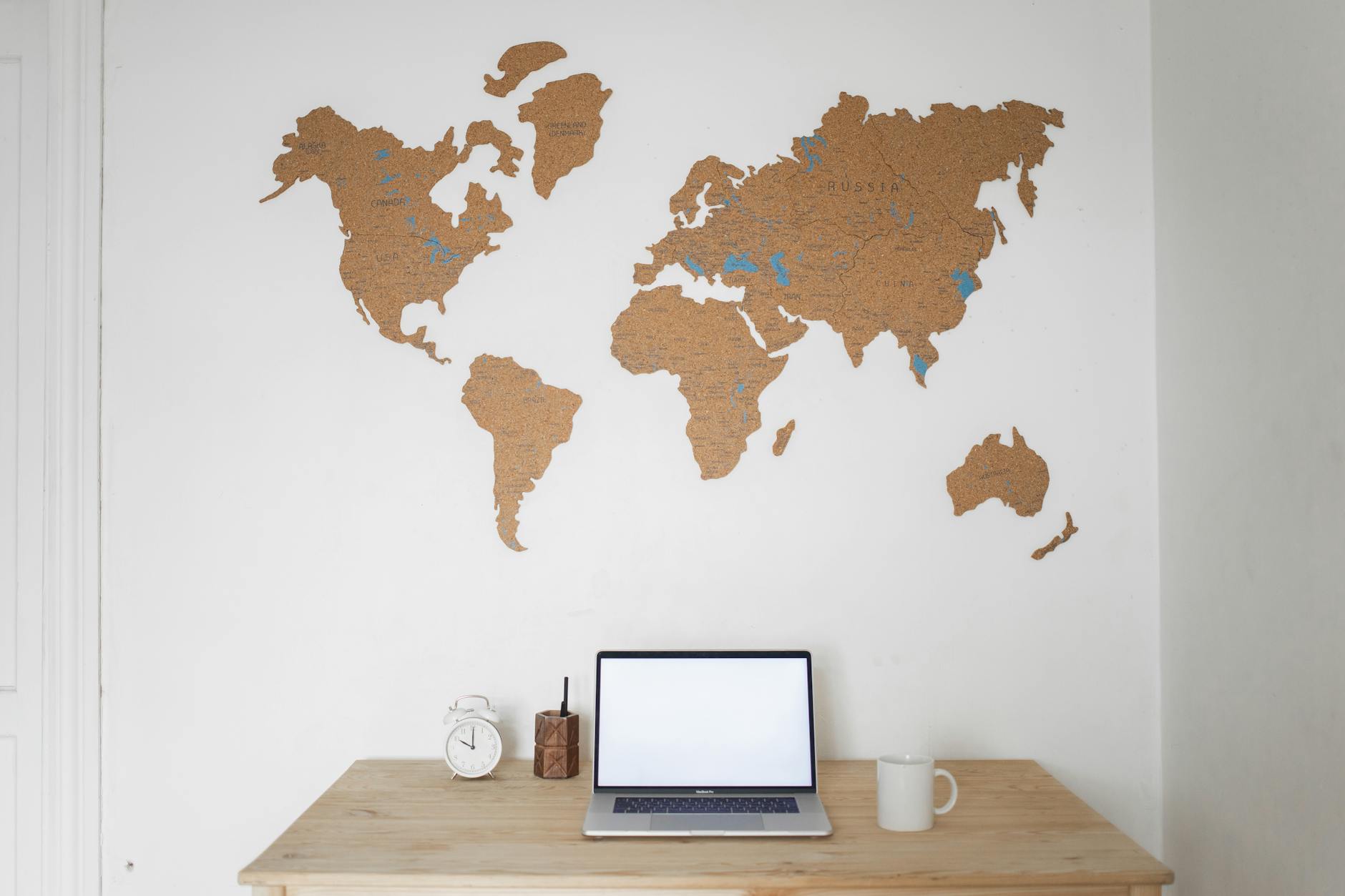 Minimalist desk setup with a laptop and world map wall art, inspiring travel and creativity.