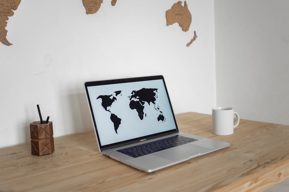 NordVPN vs ExpressVPN vs Surfshark for Privacy A minimalist desk setup with a laptop showing a world map screen and a mug, set against a wall map backdrop.
