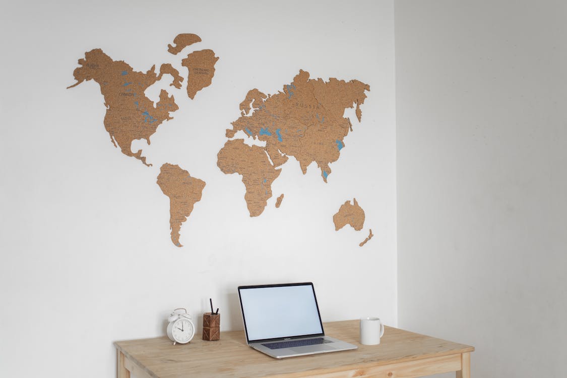 Wooden table with modern netbook with blank screen and alarm clock placed at white wall with decorative world continents in light room