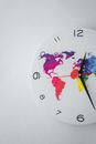 Round clock with bright world map and black Arabic numerals hanging on white background in light room of modern studio
