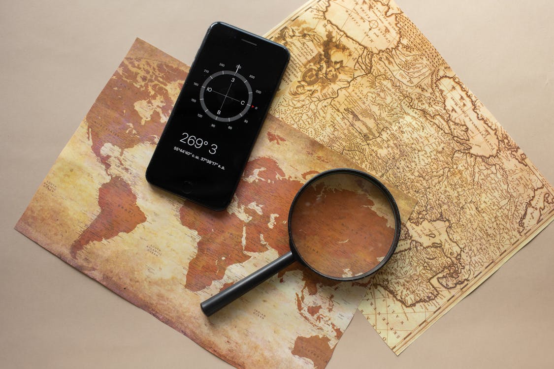 Loupe and smartphone with a compass showing latitude and longitude coordinates sitting on maps.