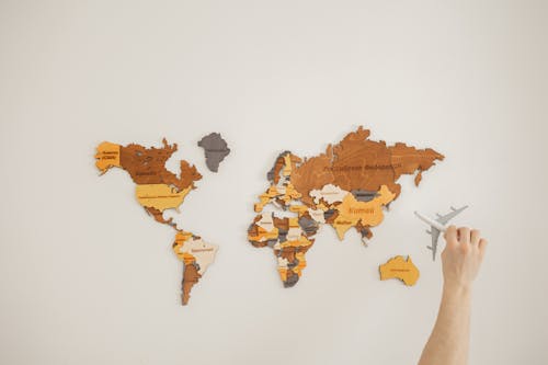Free Crop anonymous traveler with toy aircraft over decorative wooden world map with country names on white background in light room Stock Photo