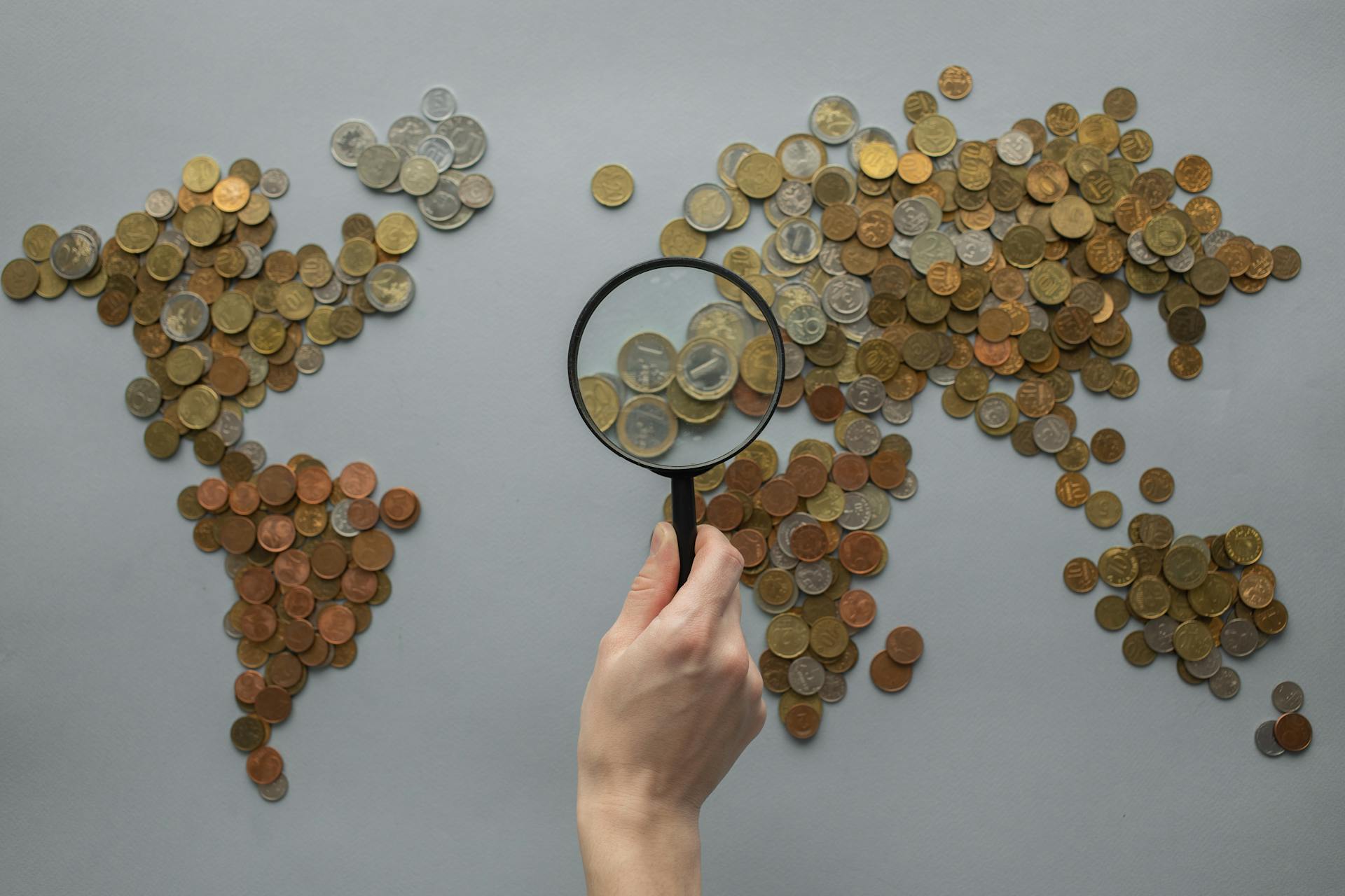 A creative world map composed of coins with a magnifying glass highlighting Europe.