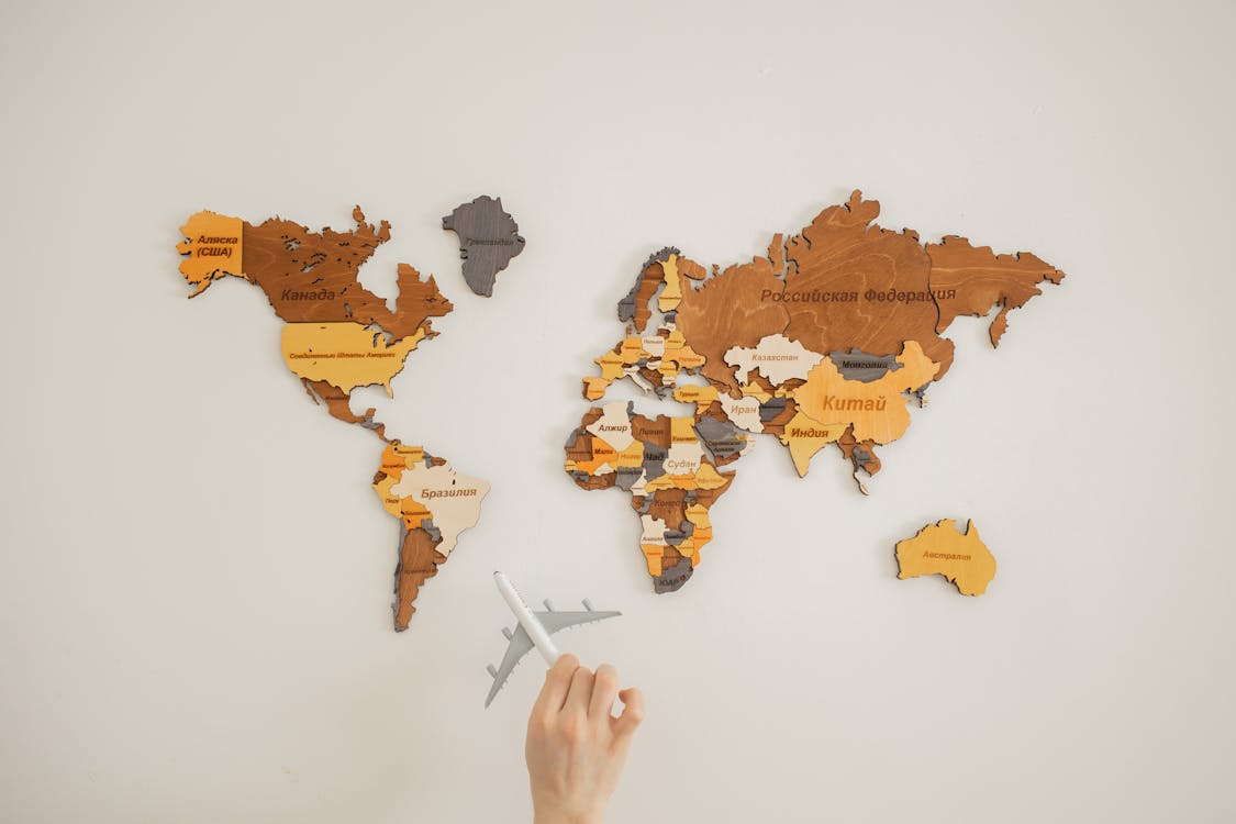 Free Crop unrecognizable person with toy aircraft near multicolored decorative world map with continents attached on white background in light studio Stock Photo