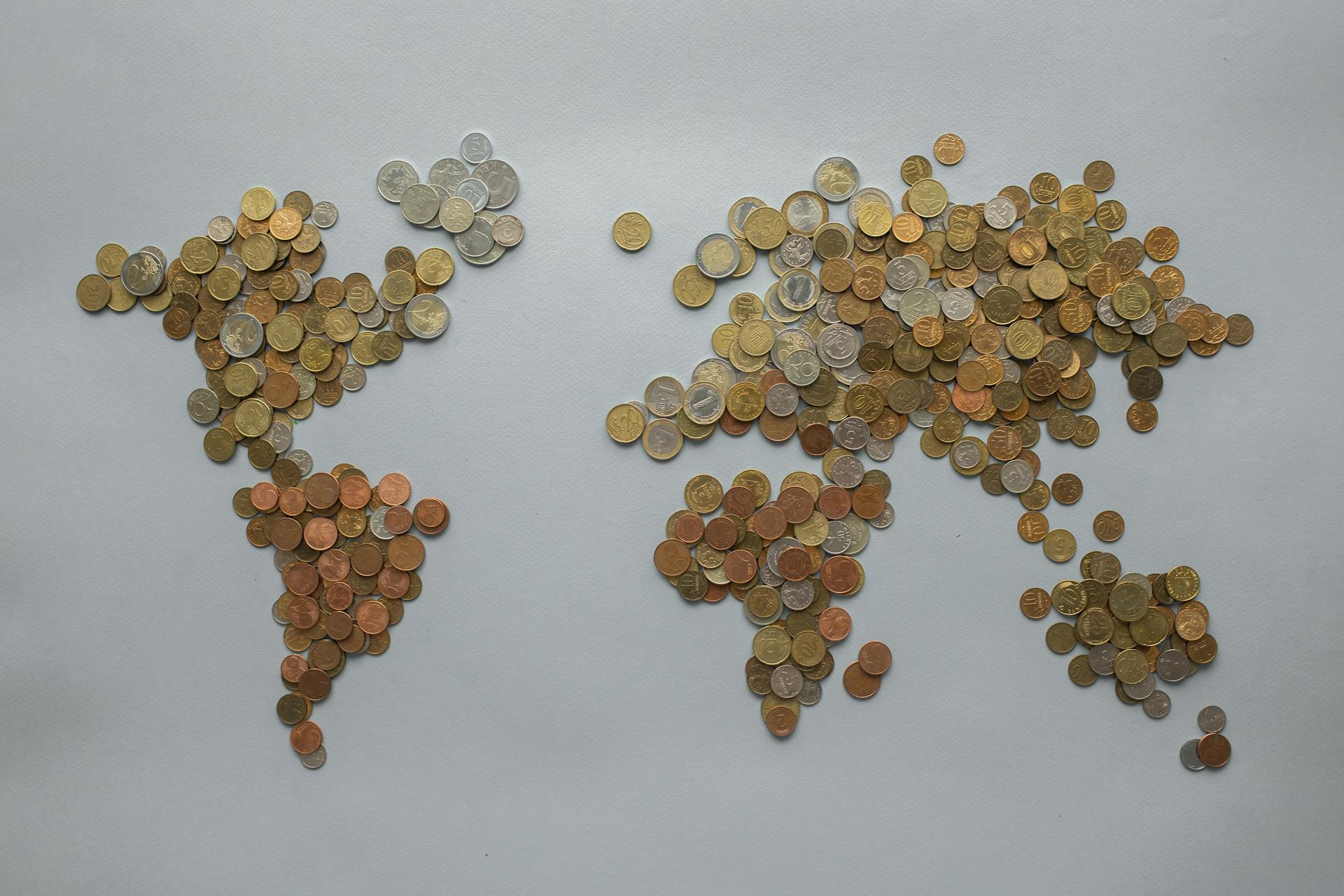 Creative world map made from assorted coins on a solid gray backdrop, symbolizing global finance.