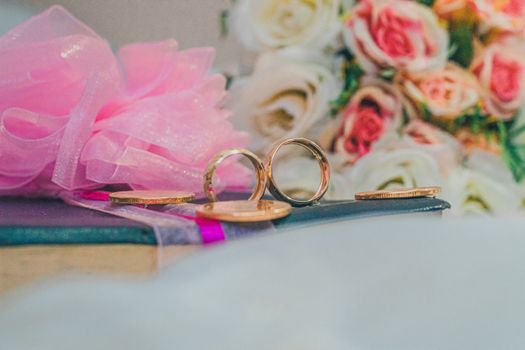 Close-up of gold wedding rings with a backdrop of roses, ideal for celebrating love.