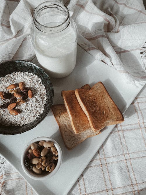 Free Tasty organic breakfast of oatmeal with nuts and toasts with milk served on tray on tablecloth on bed in morning in daylight Stock Photo