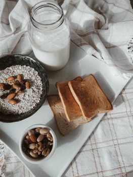 Tasty organic breakfast of oatmeal with nuts and toasts with milk served on tray on tablecloth on bed in morning in daylight